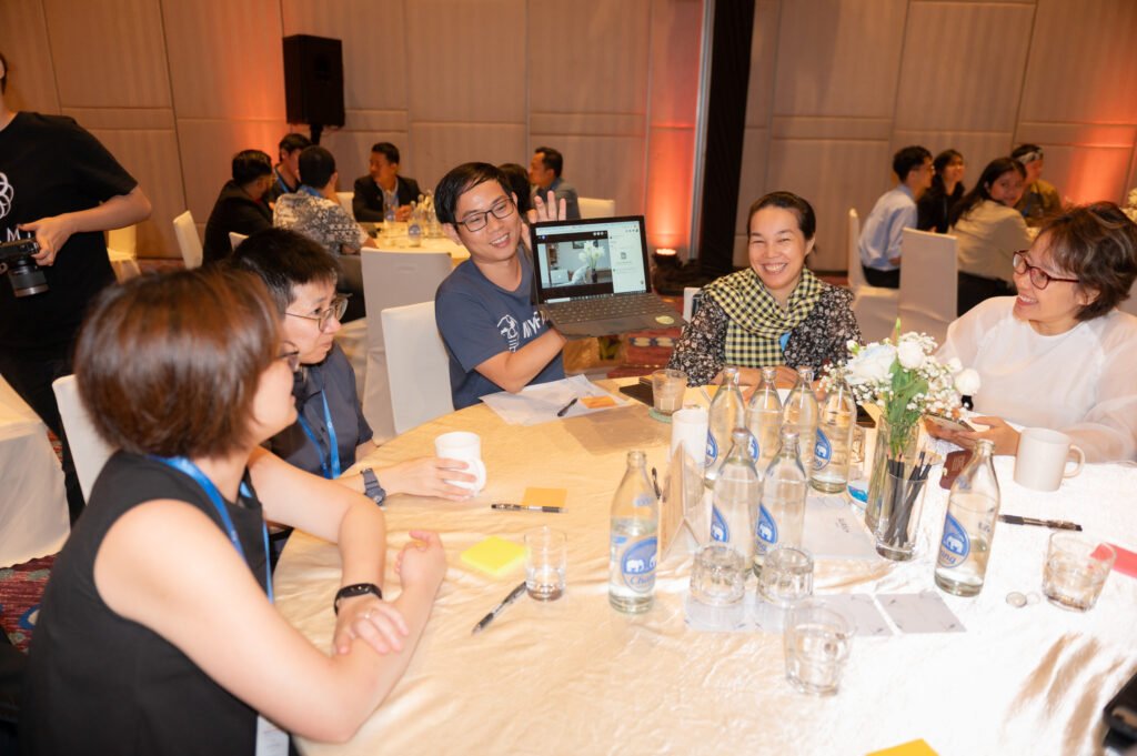 Delegates at the ASEAN SEDP 4.0 workshop collaborating around a table, with one person presenting on a laptop.