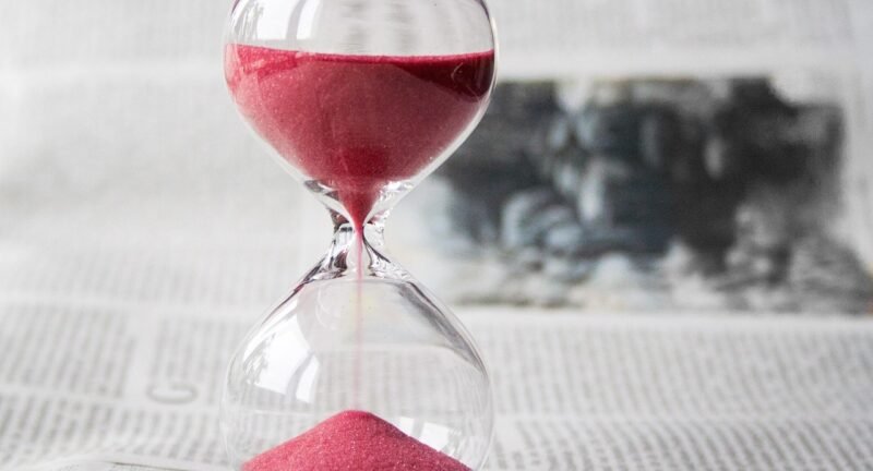 Close-up of a glass hourglass with red sand running through, symbolizing the time remaining to finish the year strong financially