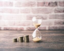 Three rising stacks of coins beside an hourglass representing compounding interest and time.