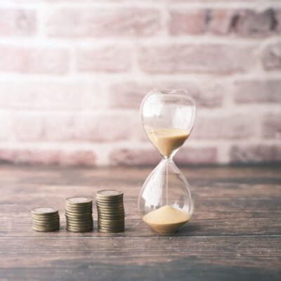 Three rising stacks of coins beside an hourglass representing compounding interest and time.