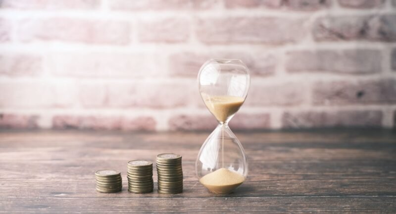 Three rising stacks of coins beside an hourglass representing compounding interest and time.